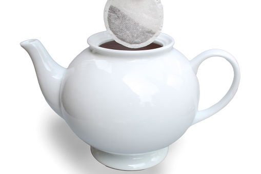 Adding a tea bag to teapot on white background