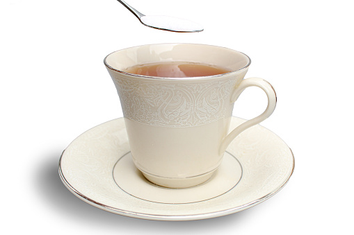 Adding a teaspoon of sugar to a cup of tea on a white background.