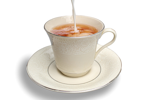 Milk being poured into cup of tea on a white background