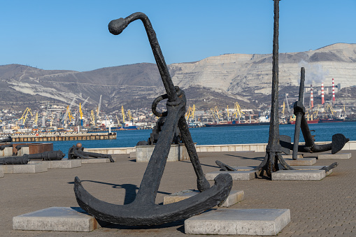 Admiralty anchor close-up in exposition of sea anchors and cannons. Serebryakov embankment. In background, berths of commercial seaport. Blurred background. Novorossiysk, Russia - December 20, 2022