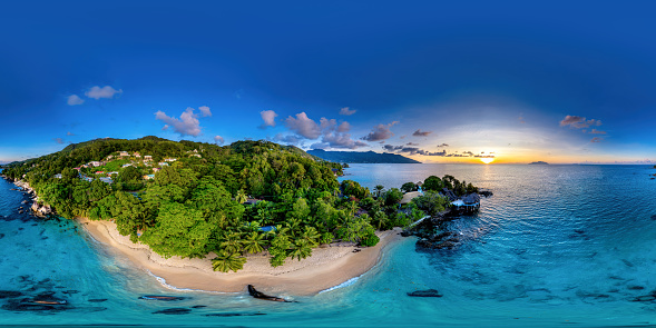 Ultrahigh resolution 360 panorama of a sunset on the beach in Mahe, Seychelles with a lush green forest.