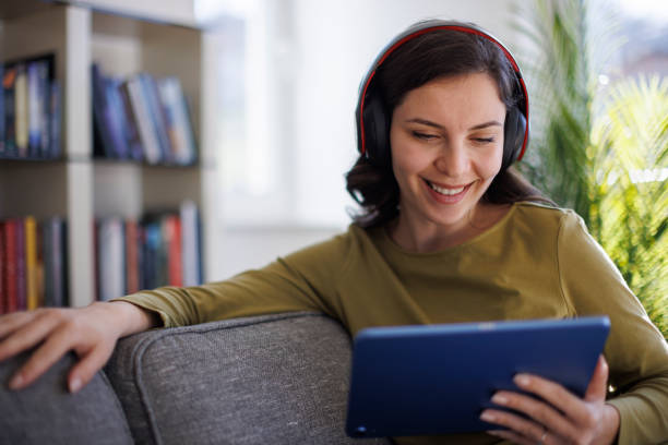 istock Smiling young woman with wireless headphones using digital tablet at home 2096737606