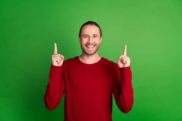 istock Photo of satisfied toothy beaming man with stubble dressed red pullover indicating at offer empty space isolated on green color background 2096763104