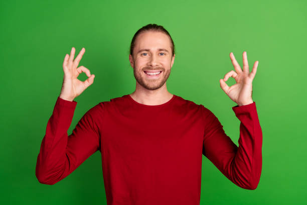 istock Photo of good mood cheerful man with stubble dressed red pullover two hands showing okey symbol isolated on green color background 2096764675