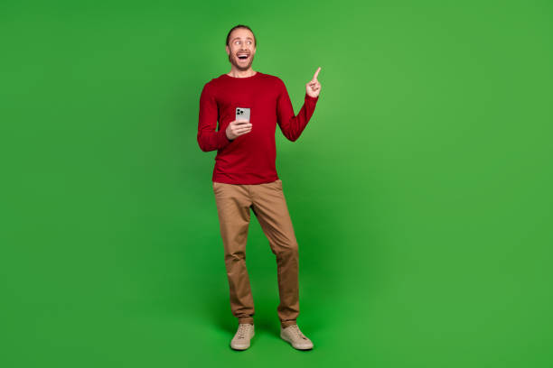 istock Full size photo of attractive man indicating look at impressive discount empty space hold smartphone isolated on green color background 2096767916
