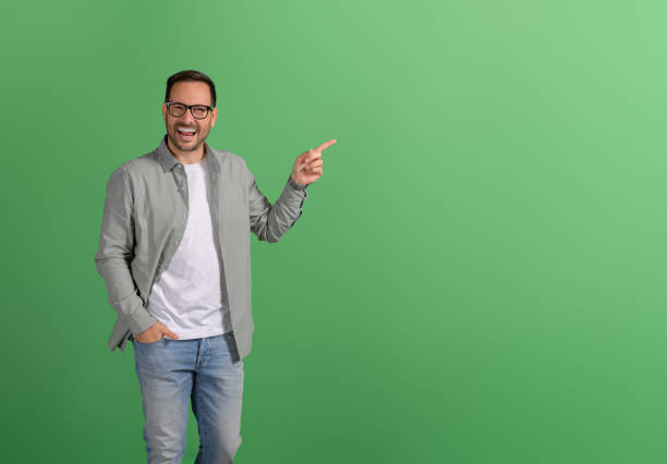 istock Handsome entrepreneur with hand in pocket aiming at empty space and advertising on green background 2096796021