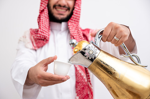 Arabian man holding arabic coffee pot wearing dishdasha and kandura on isolated white background with generosity and hospitality feelings