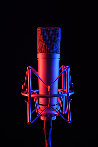 Close-up of a microphone on a black stand in neon LED lighting in blue and purple colors in a recording studio