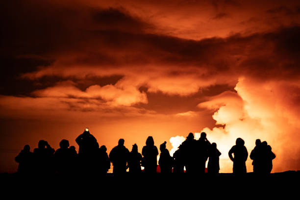 Group of people watching volcanic eruption in Iceland with a smoke and night cloudy sky