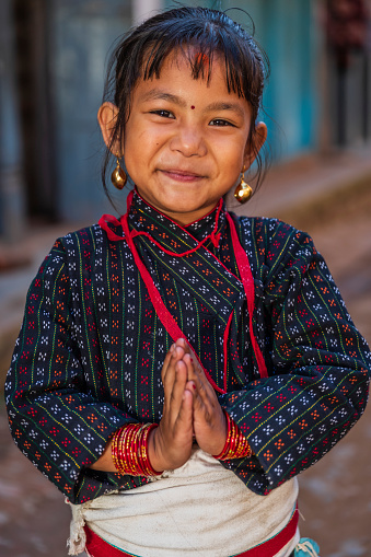 Young Nepali girl saying namaste in Bhaktapur. She is wearing traditional Newari dress. Bhaktapur is an ancient town in the Kathmandu Valley and is listed as a World Heritage Site by UNESCO for its rich culture, temples, and wood, metal and stone artwork.