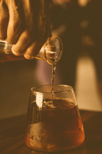 A person pouring espresso coffee into a glass jar on a table