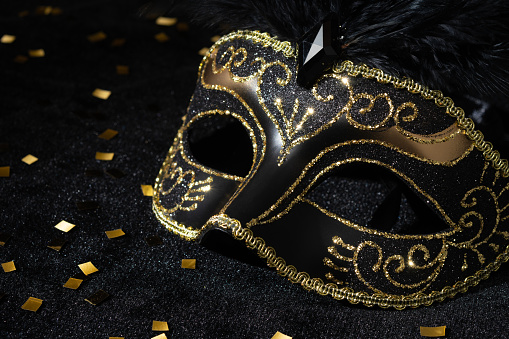 Close-up view of Masquerade gold mask with feathers and confetties on black background.