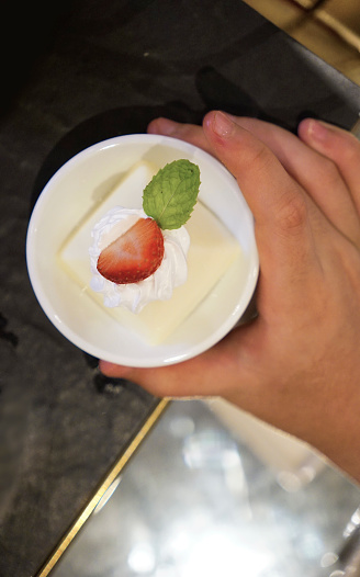 Too view of kid hand holding a panna cotta cake decorated by strawberry