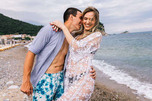 Happy young couple laughing and hugging on the beach