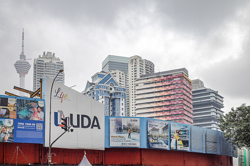 Kuala Lumpur, Malaysia - January 7th 2024:  High rise buildings from different periods including the famous communication tower behind a fence with advertisement billboards