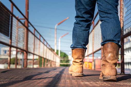 Close-up at worker feet is wearing leather safety boots during walking on rustic walkway platform. Ready to working in the challenge industrial concept scene.