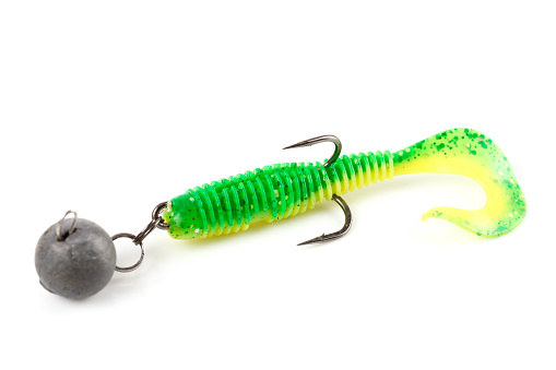 Soft fishing bait for predatory fish, green plastic grub, with double hook and lead sinker, isolated on background