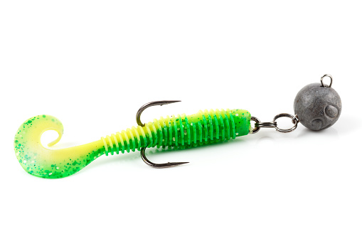 Soft fishing bait for predatory fish, green plastic grub, with double hook and lead sinker, isolated on background