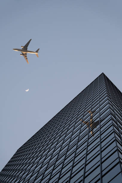 The late afternoon shot captures an airplane shortly after takeoff from Tokyo's Haneda Airport. The airplane reflects in the window facade of a skyscraper in Shibuya City district, while the rising moon is visible in the background. Truly an impressive moment.