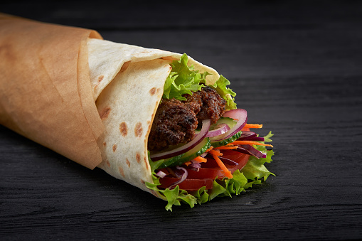 Tasty doner kebabs with fresh salad trimmings and shaved roasted meat served in tortilla wraps on brown paper as a takeaway snack.
