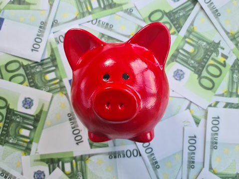 A red piggy bank is positioned on a stack of paper money, showcasing financial savings and investment. The piggy bank appears full, symbolizing financial security and wealth accumulation.