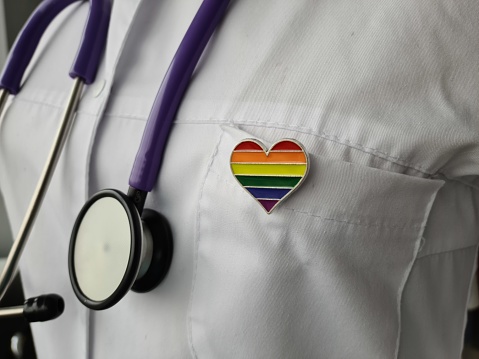 A doctors uniform featuring a rainbow heart symbol, representing diversity and inclusivity in healthcare. The uniform is white with the rainbow heart prominently displayed on the chest area.