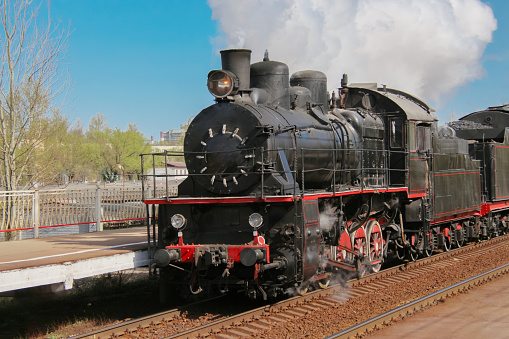 Tourist retro steam locomotive passing by the platform, releasing clouds of smoke from the chimney