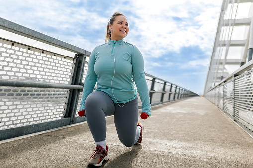 Overweight woman exercising with dumbbells on bridge