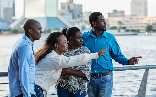 A group of four African-American friends, two couples, standing together on a city waterfront, sightseeing. They are in their 30s and 40s.