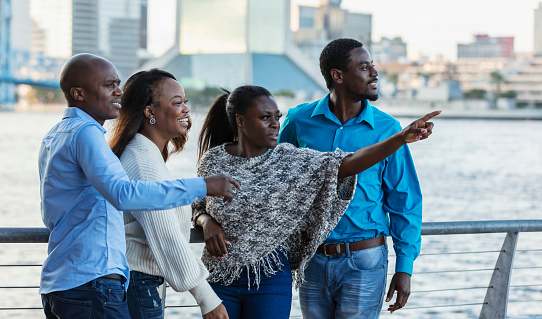 A group of four African-American friends, two couples, standing together on a city waterfront, sightseeing. They are in their 30s and 40s.