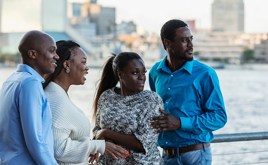 A group of four African-American friends, two couples, standing together on a city waterfront, sightseeing. The man on the right is in his 30s and his friends are in their 40s.