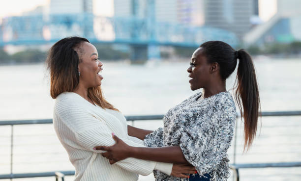 Two mature African-American woman, in their 40s, standing on a city waterfront, old friends greeting each other.