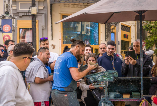 Street Artist who Paints Pictures with his Finger Surrounded by a Crowd of Curious People Watching and Recording Him Painting Street Artist who Paints Pictures with his Finger Surrounded by a Crowd of Curious People Watching and Recording Him Painting song title stock pictures, royalty-free photos & images