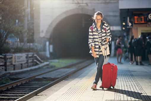 Teenage girl travelling by train. The girl is walking on platform at train station with a little suitcase.\nVernazza train station in Cinque Terre, Italy.\nNikon D850