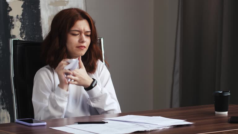 Young woman businesswoman writing article or sign on paper shits sitting at table . Crumpled papers on table around tired girl. Writing novel, letter, creating process, working concept.