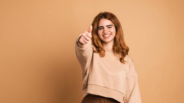 Happy woman showing thumbs up in brown studio stock photo