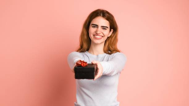 Happy young woman giving gift box in pink studio stock photo