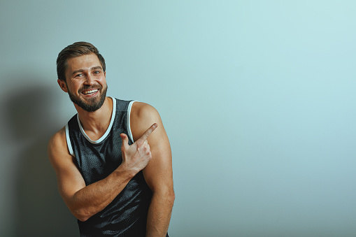 Portrait of caucasian handsome man smile wearing gray t-shirt posing against studio wall pointing with index fingers at copy space for advertisment or promotional content...