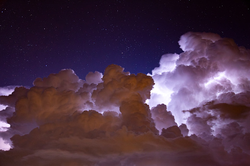 A huge nighttime thunderstorm. The lightning illuminates the clouds from within. A sprite of lightning can be seen.