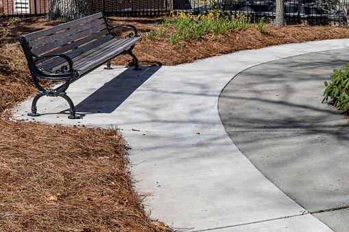 Circular concrete walkway with park bench, well tended landscaping with copy space, horizontal aspect