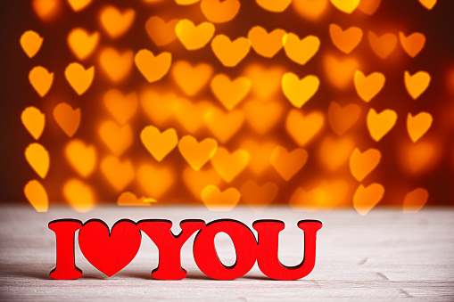 the inscription I Love You on a wooden background with beautiful hearts made of lights on a blurred background close-up
