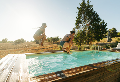 Photo of female friends jumping into the pool