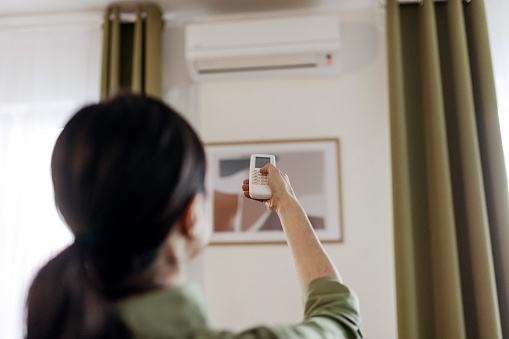 Woman Holding Remote Control Aimed at the Air Conditioner