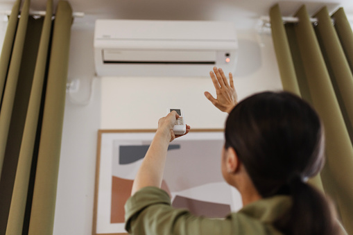 Woman Holding Remote Control Air Conditioner in House