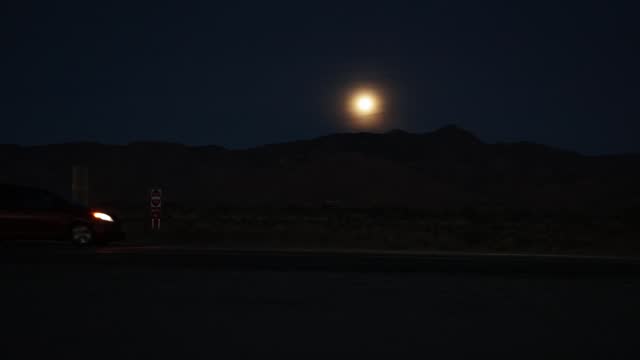 Time lapse video of moon rising over mountain range with vehicles driving by in Nevada.