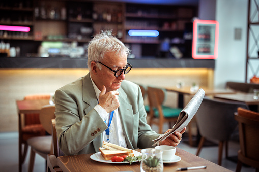 Senior businessman reading newspaper while having lunch break at cafe