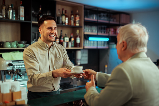 Barista giving coffee to a senior well dressed man at cafe
