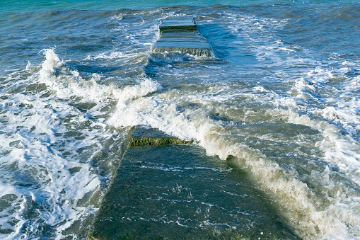Waves crash on the pier. Water splashes, drops, splash. Marine background. Beautiful seascape.