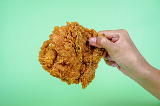 istock Female hand holding fried chicken on green background. 2097333495