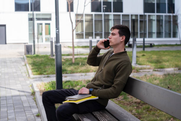 istock Young student talking on a mobile phone and sitting on a bench in a campus 2097343284